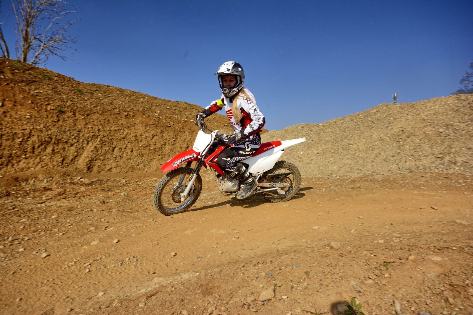 MX-Academy Österreich: Motocross-Fahrer auf Honda über einem sandigen Hügel, blauer Himmel